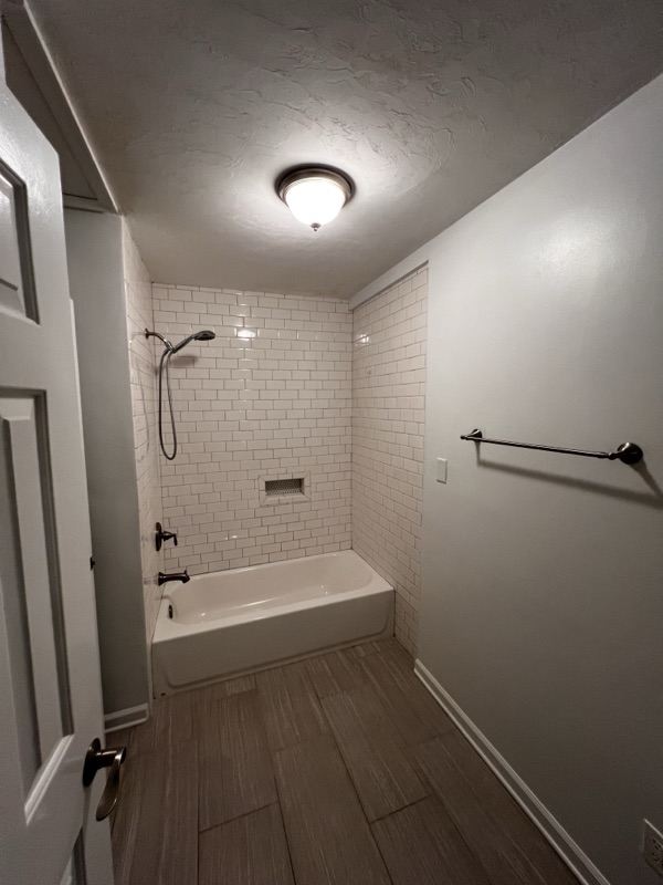 Renovated full bath with subway-tile shower surround, deep tub, and wood-look flooring