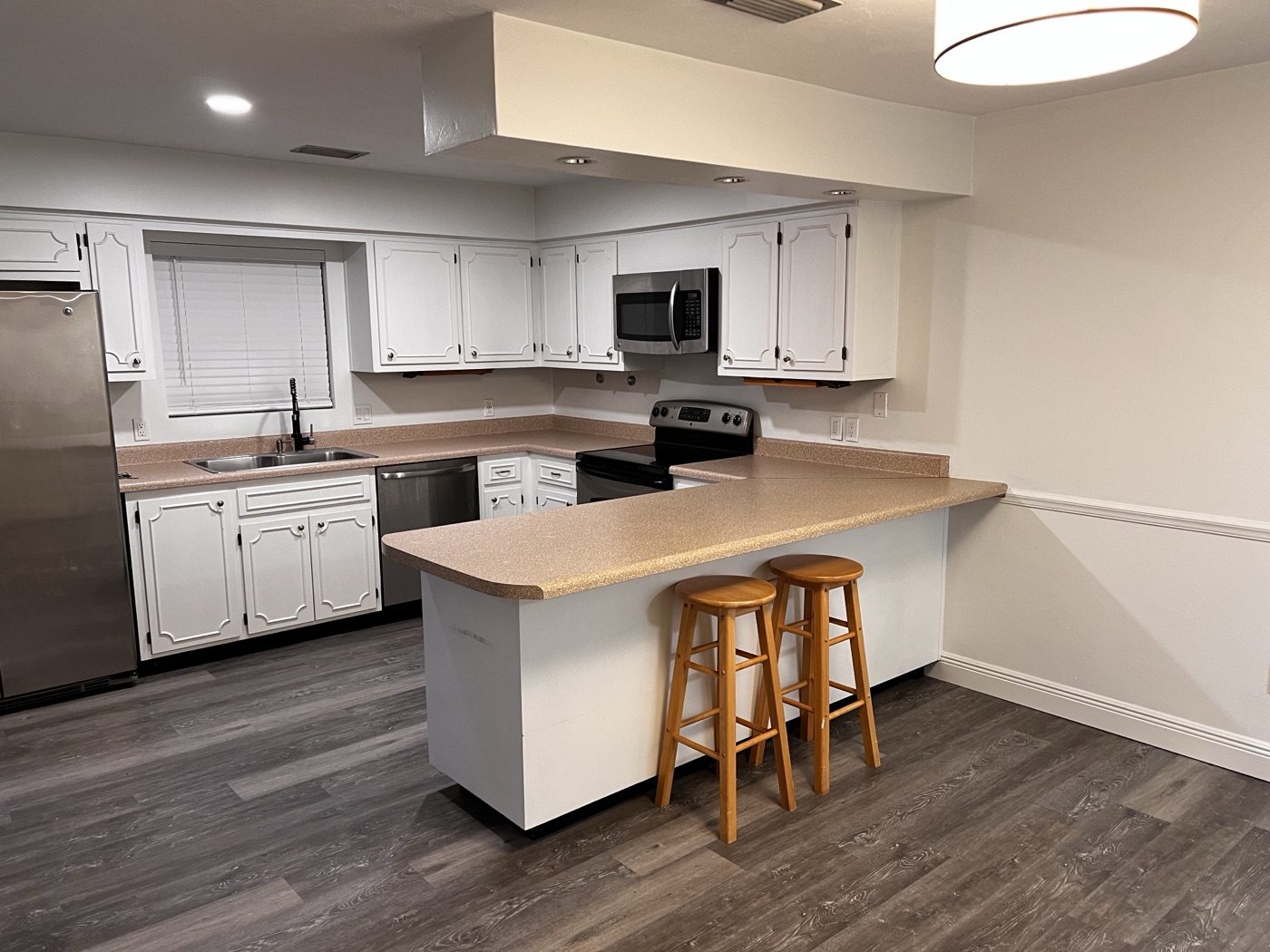 Kitchen with white raised-panel cabinets, peninsula counter with bar stools, and stainless appliances