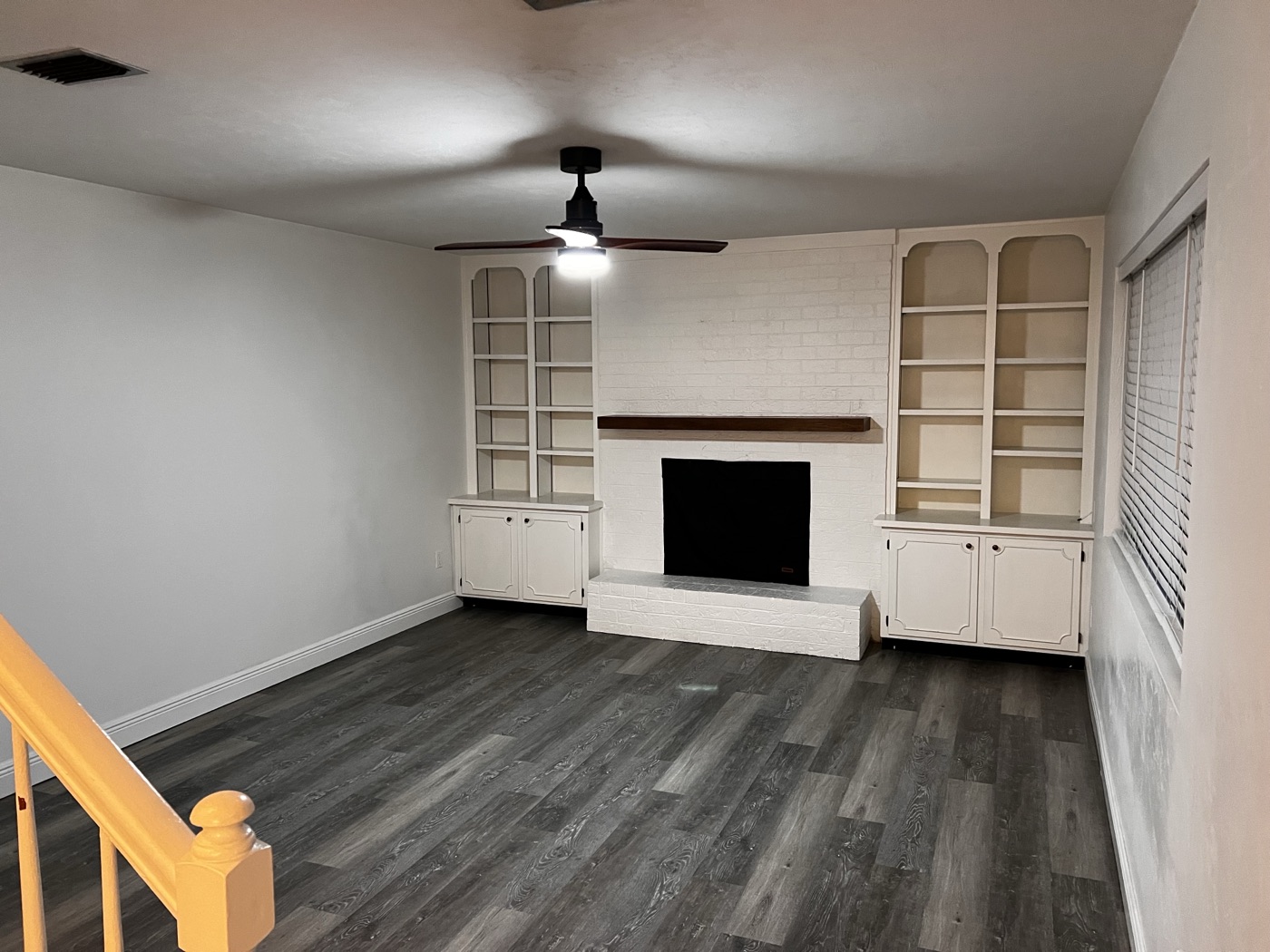 Living room with white-painted brick fireplace, arched built-in shelves, and dark wood-look flooring